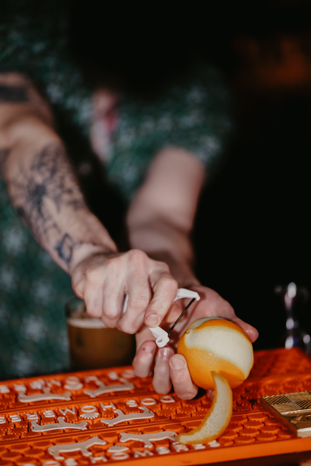 A tattooed bartender cutting an orange peel over the service mat
