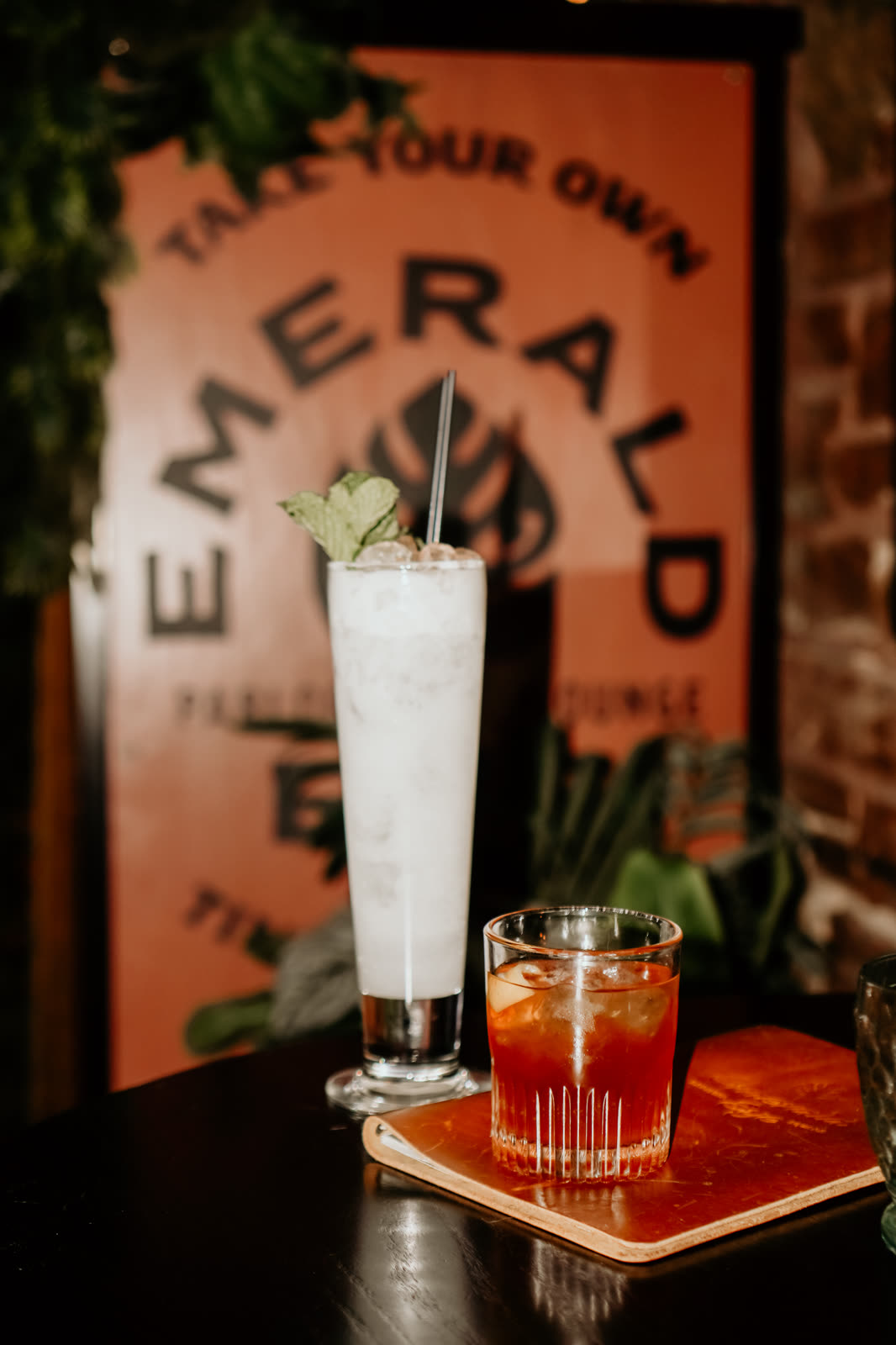 Two cocktails on a table in front of the painted Emerald Eye sign