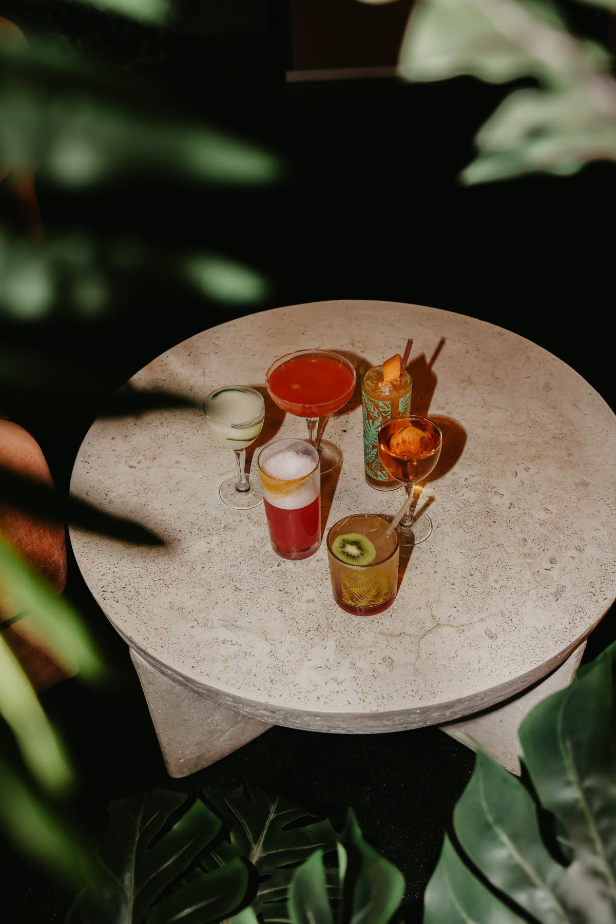 Five cocktails set out on a low stone table surrounded by plants in the lounge